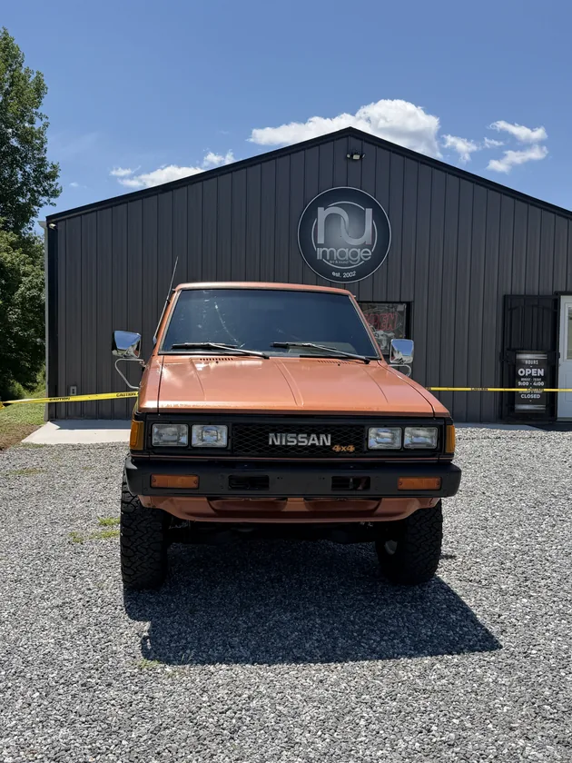Orange Nissan 720 4x4 pickup head-on outside the NU-Image shop