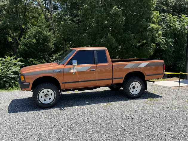 Orange Nissan 720 King Cab pickup on white wheels with tinted windows